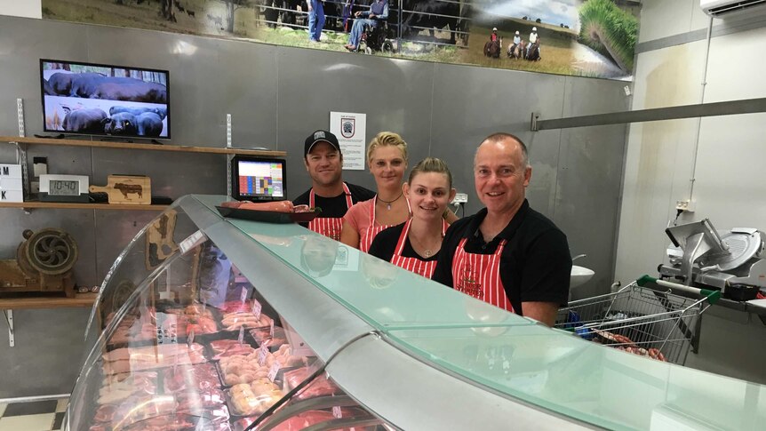 Four butchers stand behind the meat counter