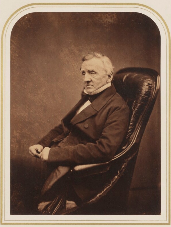 A portrait of a man dressed in a suit sitting in a leather chair.