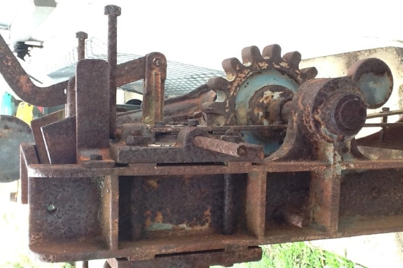 A rusty piece of machinery showing a big cog, levers and rectangular shaped sections. 