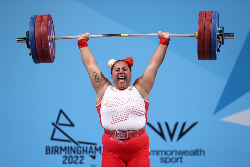 An English weightlifter closes her eyes and shouts out as she locks her arms to complete a lift at the Commonwealth Games.