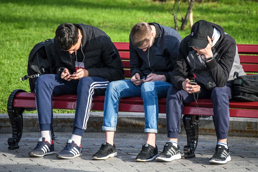 Russian teenagers use their mobile phones while sitting on a park bench