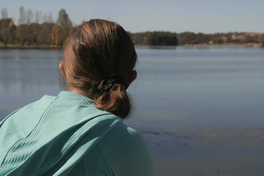 A woman looks at a lake, her face his hidden
