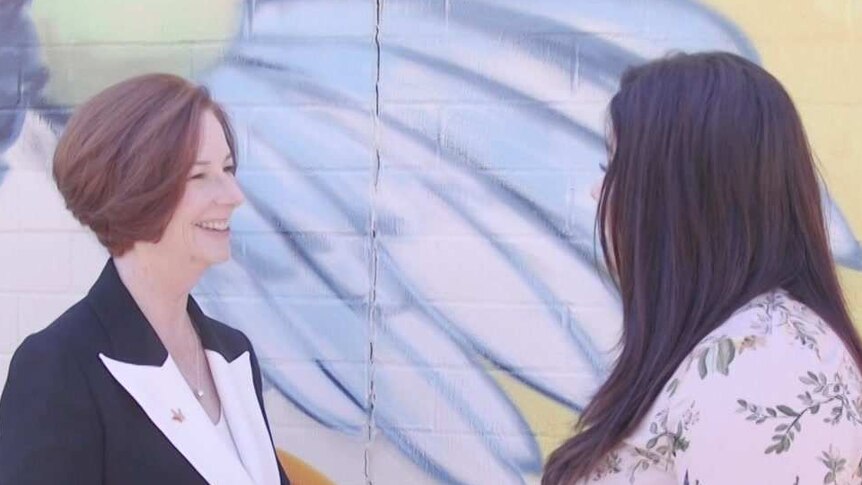 Julia Gillard speaks to a woman whose face is obscured by her hair. They stand in front of a mural