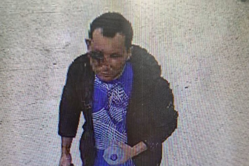 A security camera still of a man with an injury to his eye carrying a bottle of water