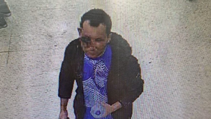 A security camera still of a man with an injury to his eye carrying a bottle of water