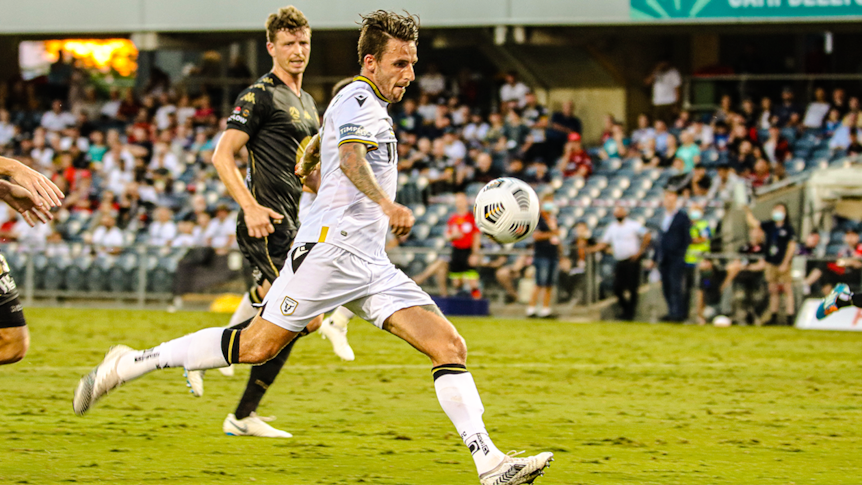 A footballer in a white jersey and white shorts kicks the ball during a match.