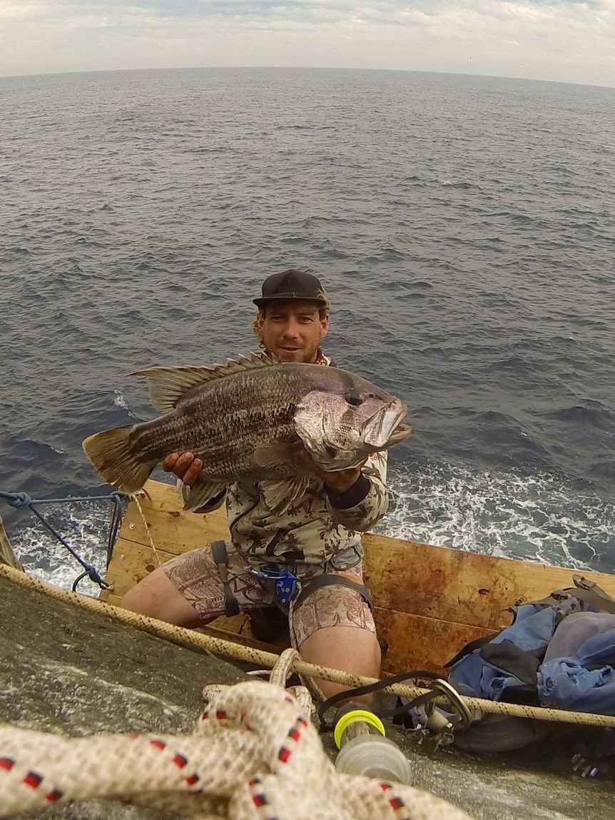 A man holding a large fish on a wood platform over the ocean
