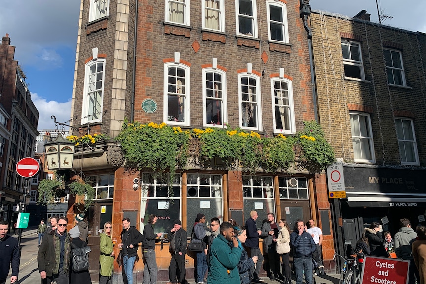 A group of people stand in a line outside a British pub.
