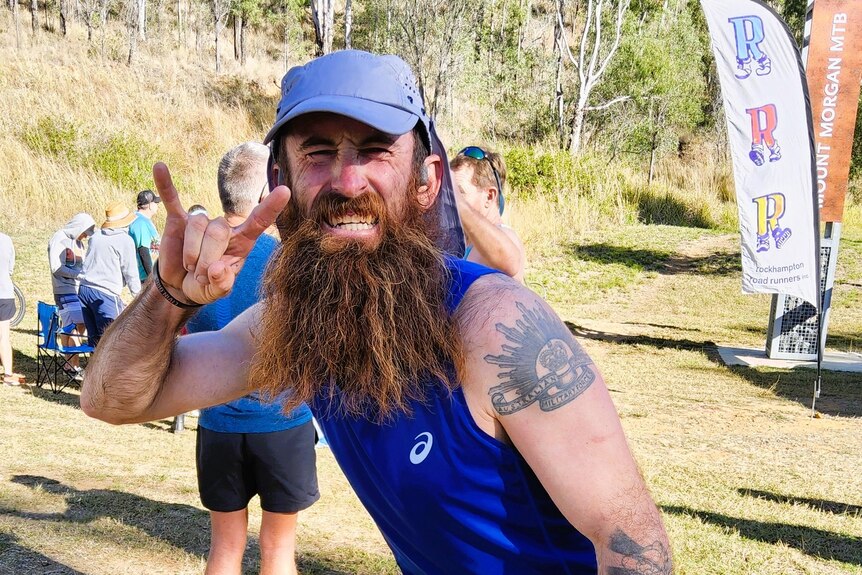 A man a long brown, ginger beard wearing in a blue singlet and light blue hat at a mountain run.