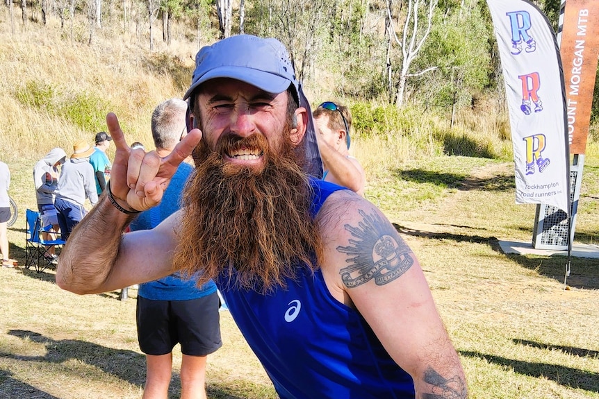 A man a long brown, ginger beard wearing in a blue singlet and light blue hat at a mountain run.