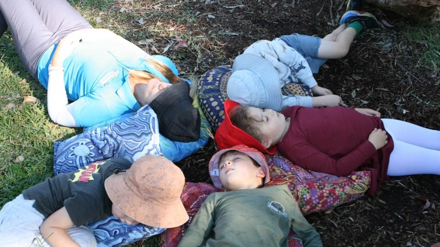 Kids and one adult lying on the ground outside
