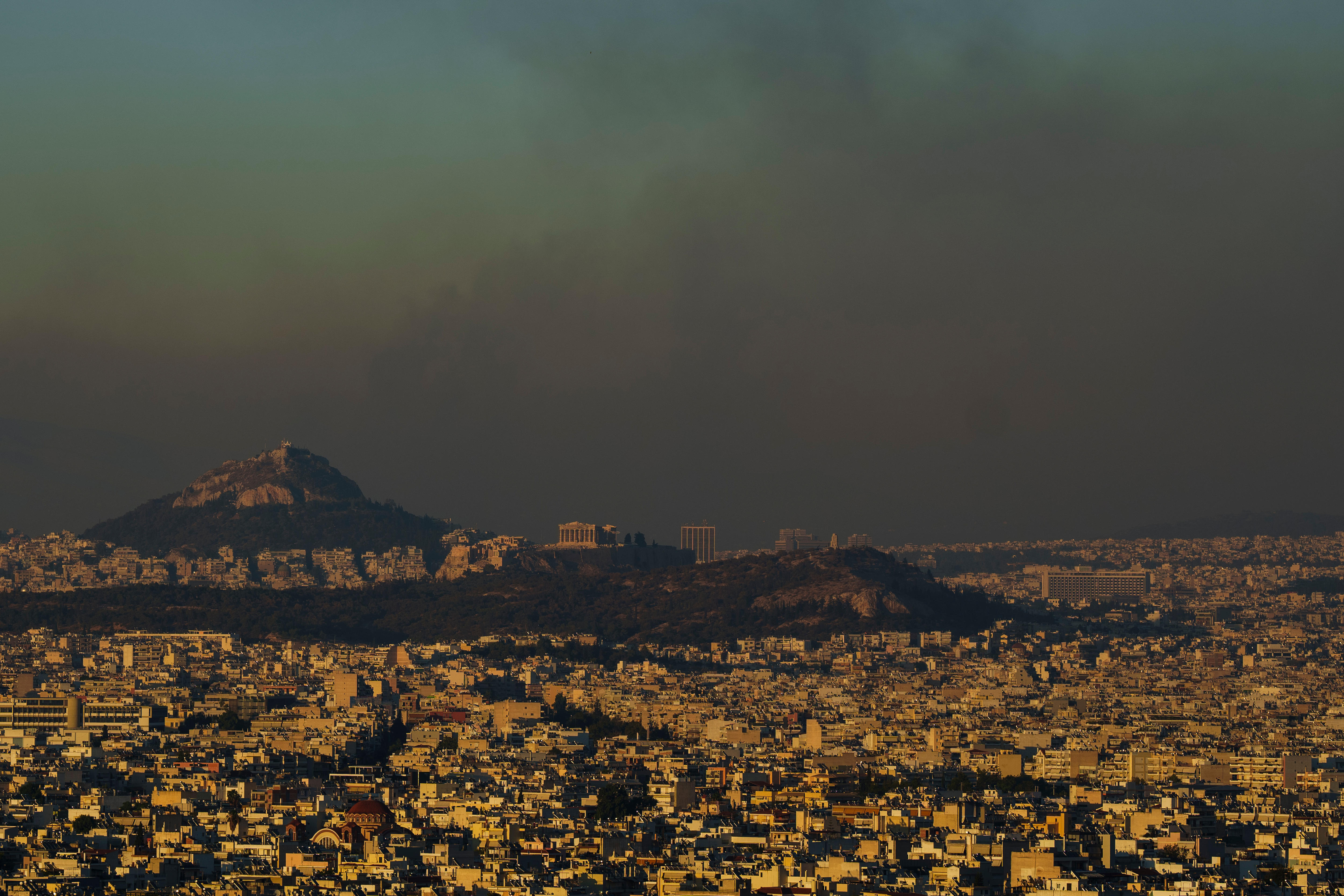 A wide shot of the Athens skyline, including the Acropolis hill, covered in smoke.