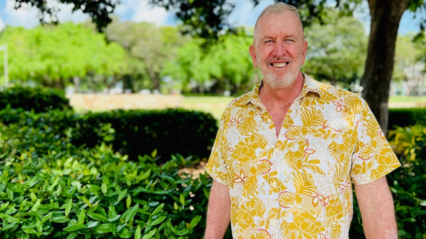 Man smiling in tropical yellow shirt stands outside in front of park