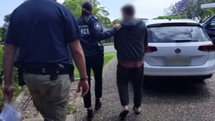 Federal police escort an unidentifiable man down the driveway of a suburban home.