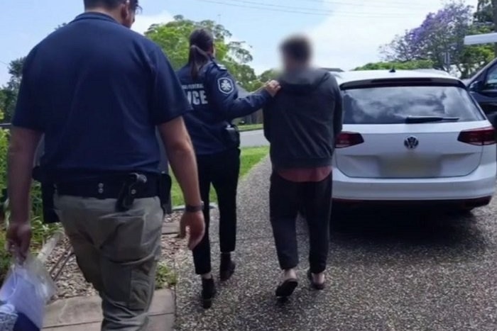 Federal police escort an unidentifiable man down the driveway of a suburban home.
