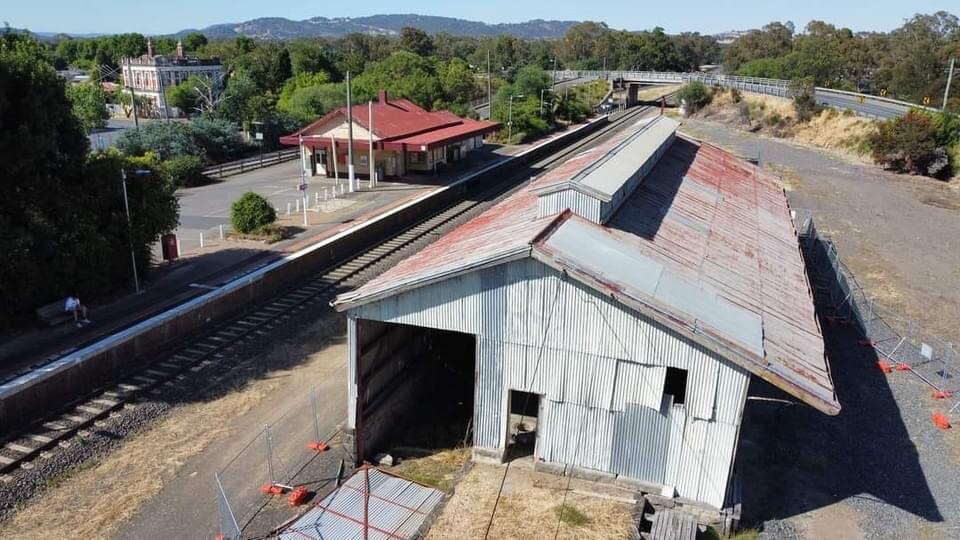 An aerial photo of an old shed next to a railway track with another building in the background