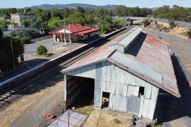 An aerial photo of an old shed next to a railway track with another building in the background
