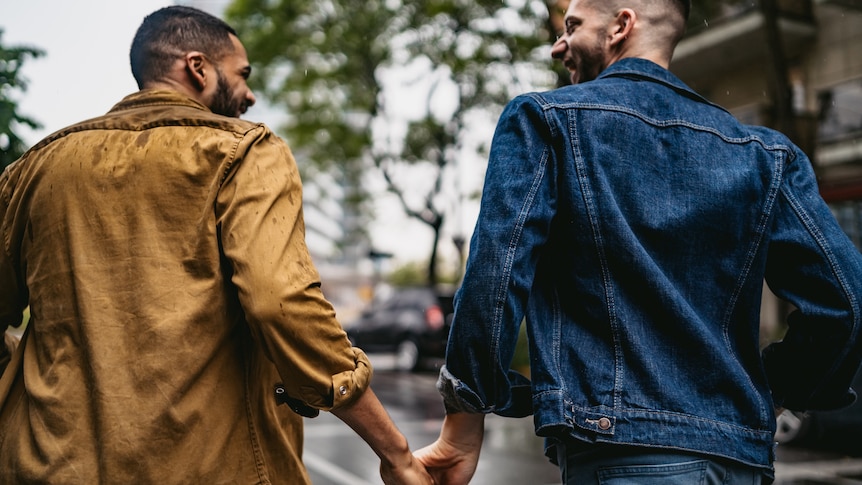 A male queer couple holding hands and sharing a laugh while crossing the road