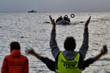 Volunteers gesture to guide refugees and migrants on a dinghy
