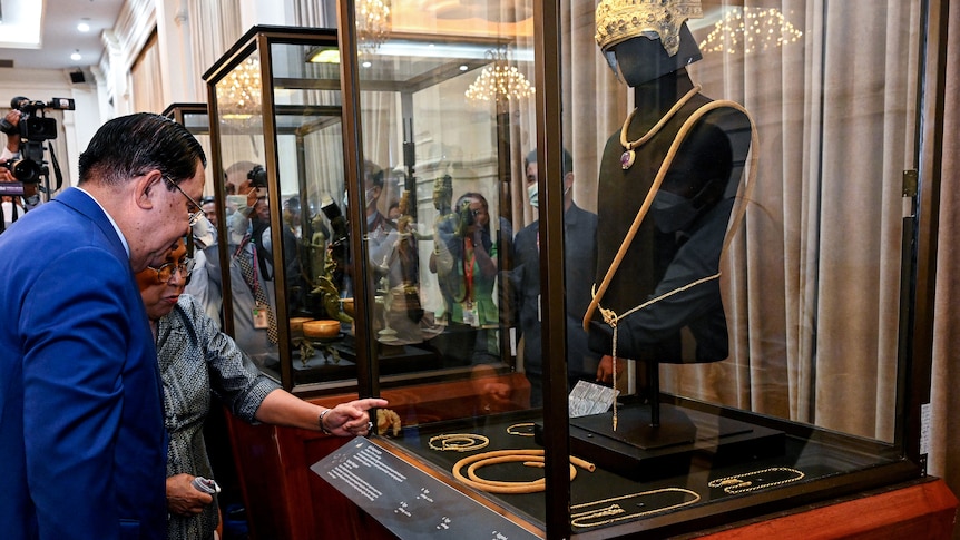 A man wearing a suit is looking at jewellery on display behind glass.