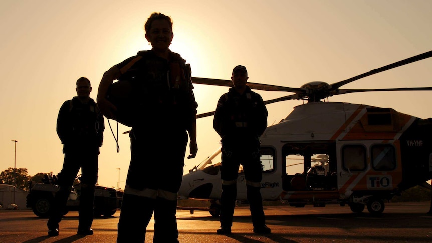 Three CareFlight workers stand in front of a helicopter at sunset.