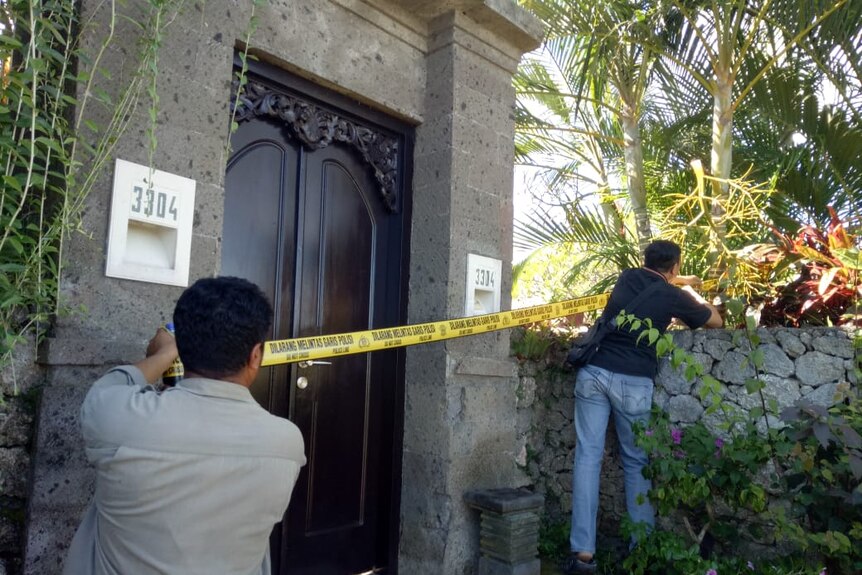 Two men stretch yellow police tape across a large wooden door in an stately building.