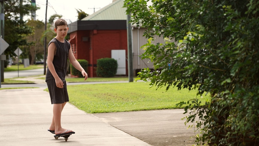 a 12 year old boy rides on a board down a quiet residential street