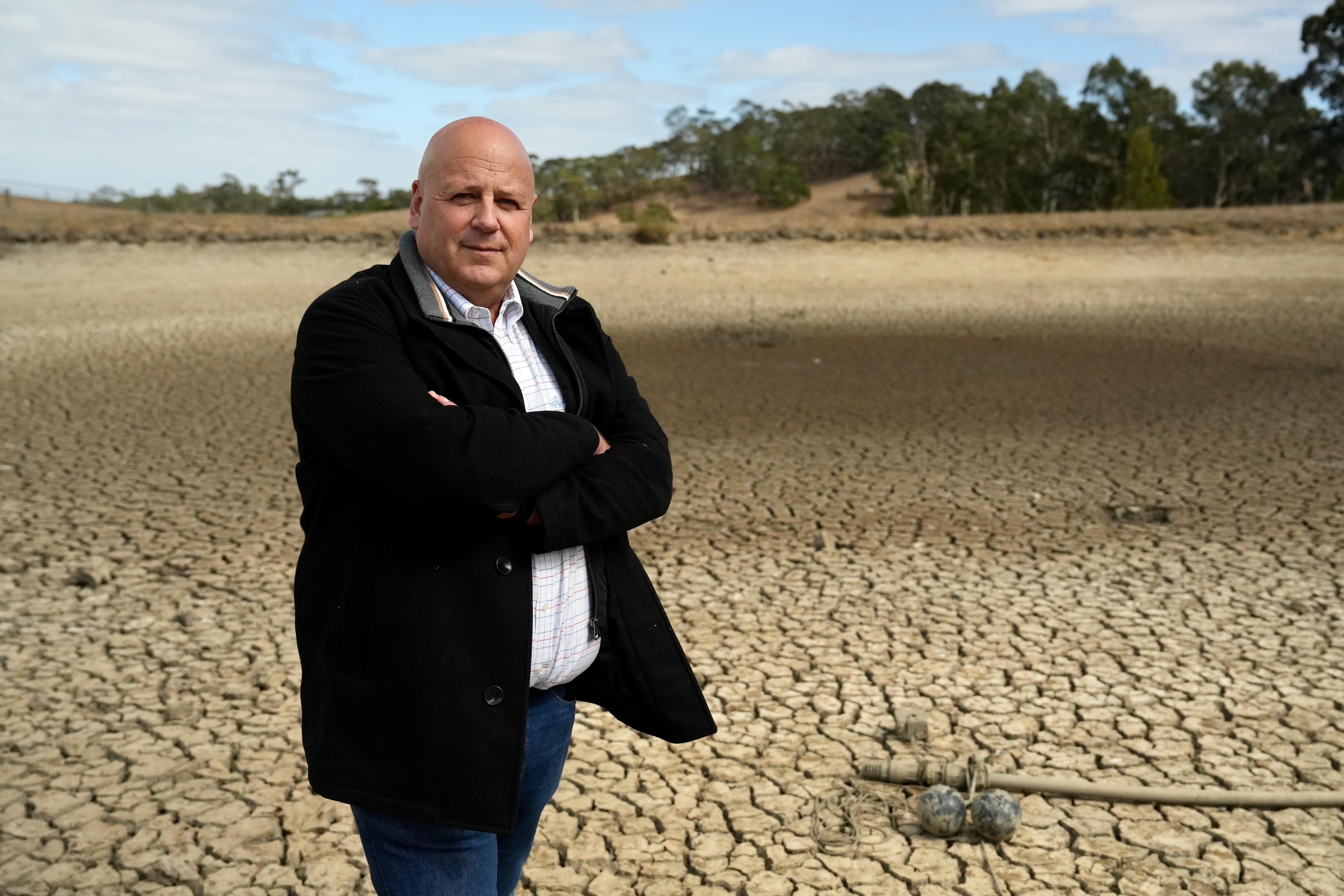 Мужчина в джинсах, белом топе и куртке стоит на сухой дамбе.