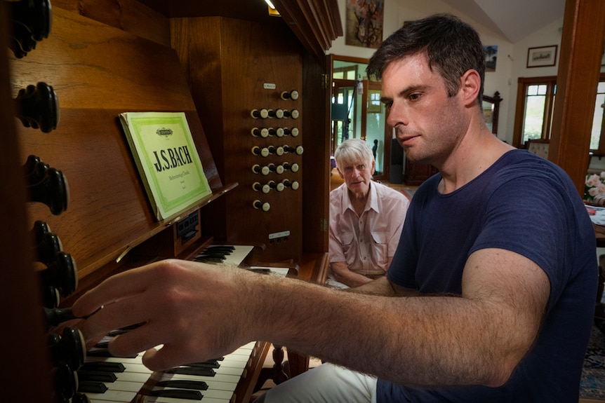Man playing a wooden organ with an older man looking on