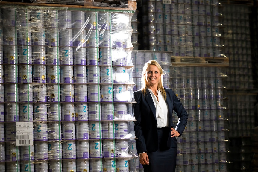 A woman in a suit stands in front of tins of baby formula