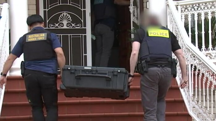 two police officers carrying a black case into a house