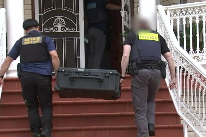 two police officers carrying a black case into a house