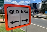 A white sign with a bright orange border, one half says Qld, the other NSW.