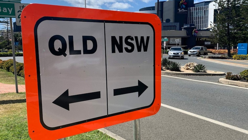 A white sign with a bright orange border, one half says Qld, the other NSW.