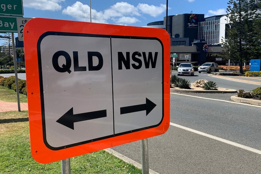 A white sign with a bright orange border, one half says Qld, the other NSW.