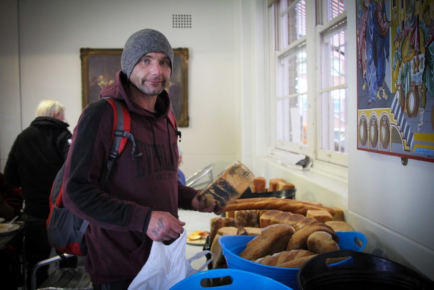 A man holding a load of bread, near a table full of bread.