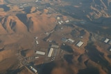 An aerial photograph shows brown desert peaks with silver industrial warehouses dotting a valley.