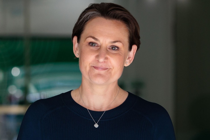 A woman in a navy blue dress emerges from a door way with a slight smile. 