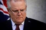 Scott Morrison frowns while looking down. He is wearing an Australian flag pin on his lapel