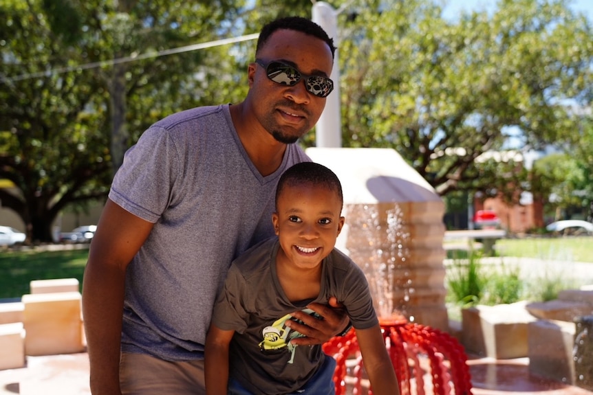 A man and his son pose for a family photo in an outdoors setting