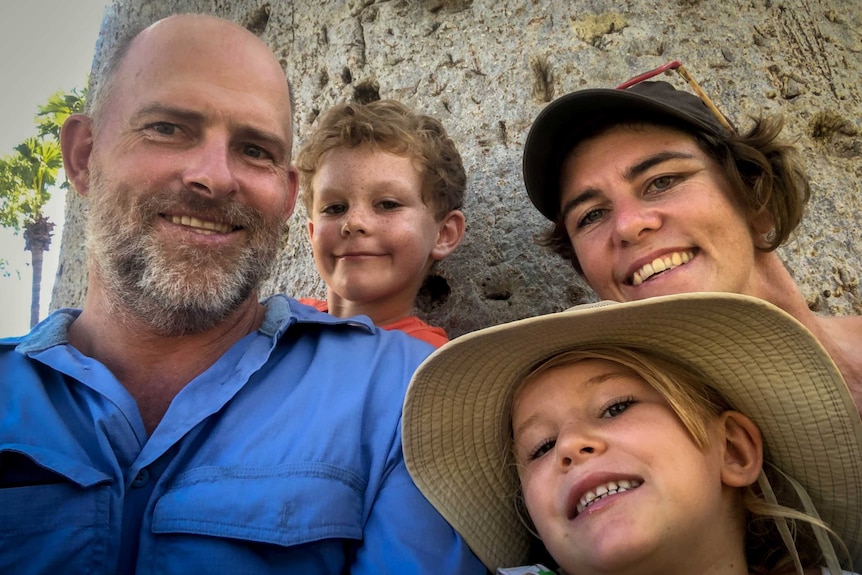 Man in blue shirt, child in orange tshirt, young girl in hat, woman with brown hair, hat, sunglasses in front of boab tree.