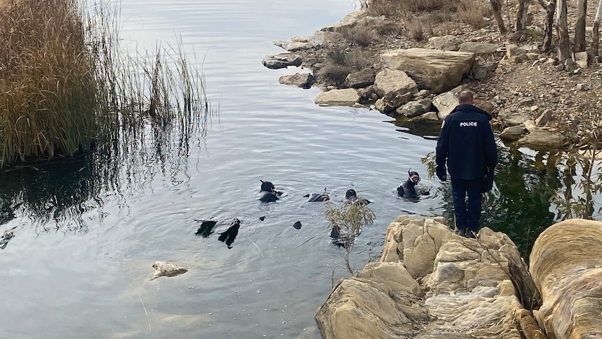 Police divers in a dam while another police officer watches