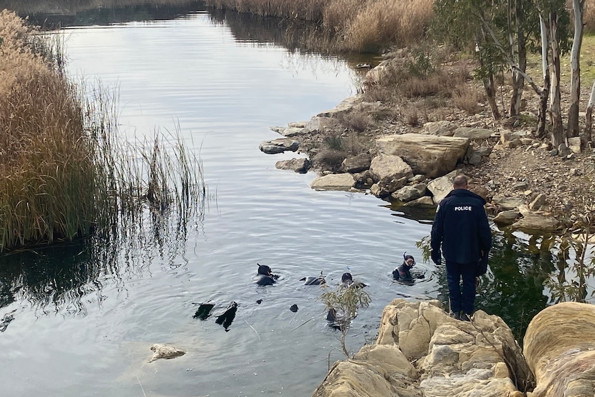 Police divers in a dam while another police officer watches