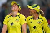 Two women in bright yellow cricket uniforms smile and laugh