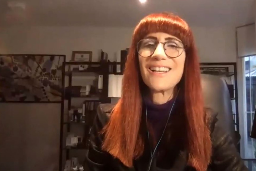 Interior headshot of a red-haired woman with glasses.