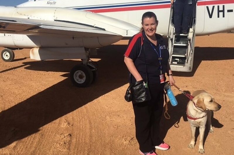 A woman with a guide dog in front of a plane.