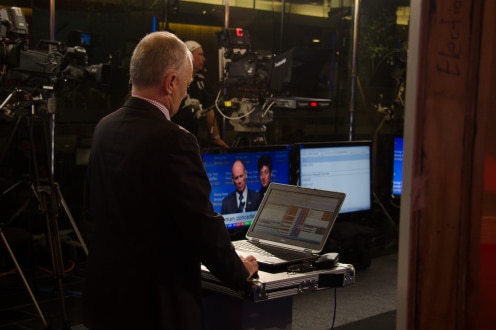 Antony Green stands in front of a computer screen in studio during election broadcast.