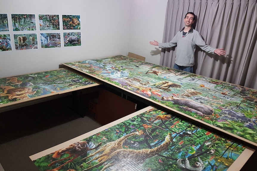 Man stand with large jigsaw puzzle he has completed.