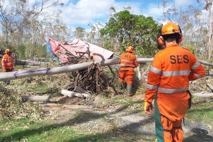 Tres voluntarios del Servicio de Emergencia del Estado de Queensland ayudan a despejar un camino después del paso de un ciclón