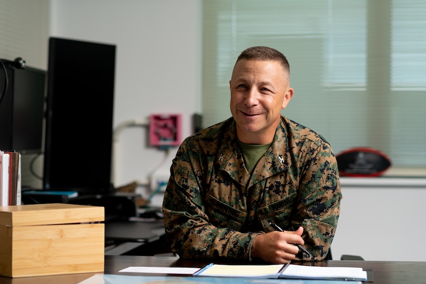A male colonel in army uniform smiles at an office desk